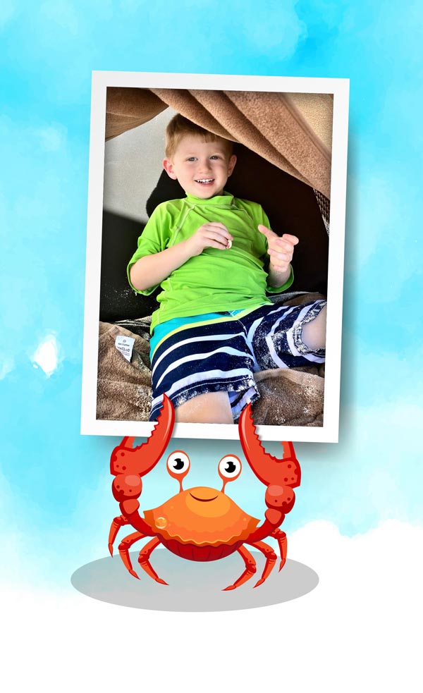 A picture of a boy (Jax) on a beach towel, held by a crab